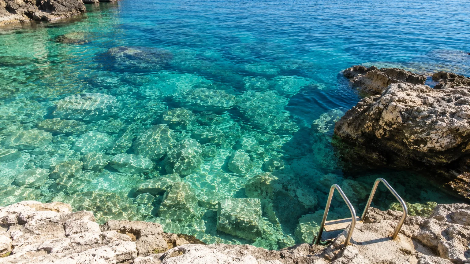 Klares Wasser über Felsgrund mit Badeleiter an der Felsküste
